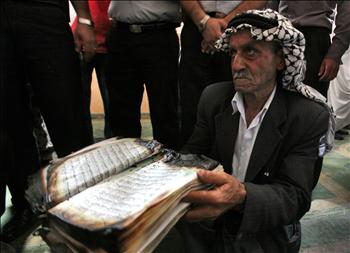 فلسطيني يحمل مصحفاً محروقاً في المسجد الذي أضرم فيه المستوطنون النار في بلدة بيت فجار في الضفة الغربية أمس