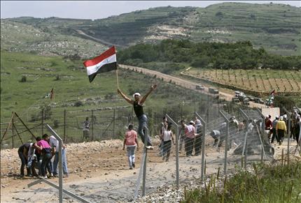 متظاهر يرفع العلم السوري فوق السياج الحدودي قرب مجدل شمس في الجولان المحتل أمس (أ ب) 
