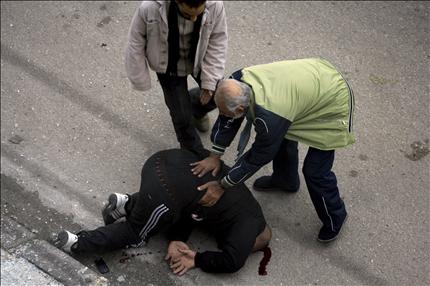 سوريان يساعدان جريحاً أصيب بسقوط قذيفة على وفد صحافي في حمص أمس (أ ف ب) 