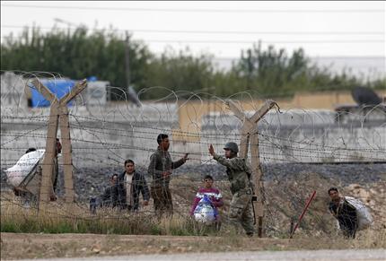 جندي تركي يمنع أهالي بلدة رأس العين السورية من عبور الحدود إلى تركيا أمس (رويترز) 