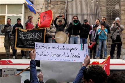 محتج يحمل لافتة كُتب عليها «في سوريا ننشد السلام والحب والحرية» فيما يظهر علم «جبهة النصرة» خلال تظاهرة في حي بستان القصر في حلب أمس (رويترز) 