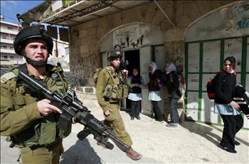 جنديان للاحتلال يمران قرب طالبات فلسطينيات خلال مواجهات في الخليل أمس