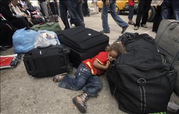 طفلة فلسطينية تنام بين الأمتعة خلال انتظارها وعائلتها عبور معبر رفح إلى مصر أمس.