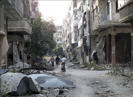 سوريون يسيرون وسط شارع مدمر في حمص امس الاول (رويترز) 