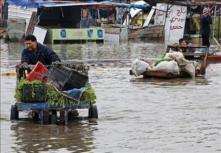 بائع جوّال يجر عربته في شارع غمرته المياه نتيجة تساقط الأمطار الغزيرة في بغداد أمس (أ ب) 