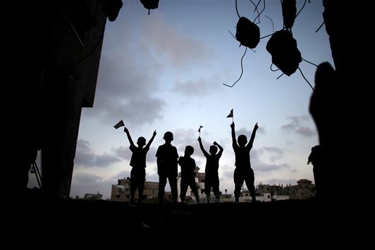 أطفال فلسطينيون يرفعون الأعلام وهم يقفون على ركام منزلهم المدمر في حي الشجاعية في غزة أمس (أ ف ب)