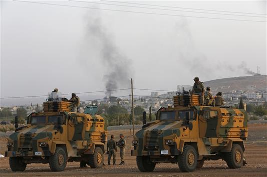 آليتان عسكريتان وجنود اتراك على الحدود السورية فيما الدخان يتصاعد من عين العرب جراء قصف «داعش» لها امس (رويترز)