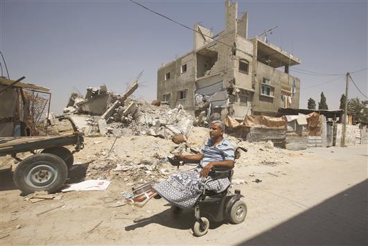 فلسطيني معوق يسير قرب منزل مدمر في غزة امس الاول (رويترز)