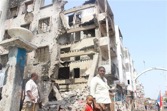 يمنيون يمرون قرب مبنى مدمر جراء المعارك التي شهدتها مدينة عدن الجنوبية، أمس (رويترز)