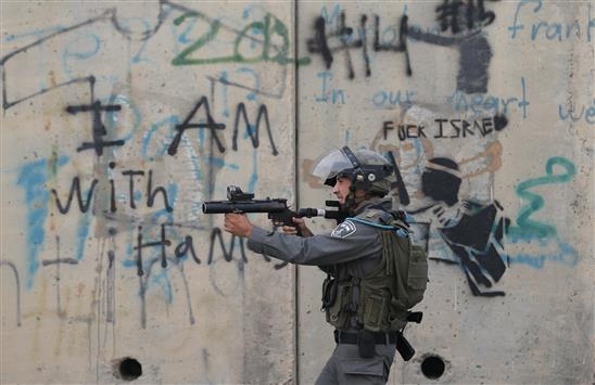 جندي إسرائيلي يصوب سلاحه في اتجاه متظاهرين فلسطينيين خلال مواجهات في الضفة الغربية المحتلة، أمس (رويترز)