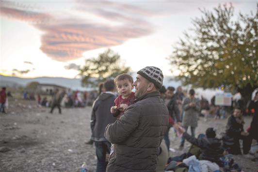لاجئ يحمل طفله وينتظر دوره أمام مركز لتسجيل اللاجئين بعد دخوله مقدونيا أمس من اليونان (أ ف ب)
