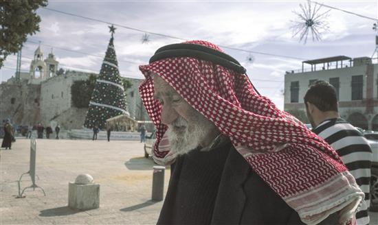 مسن فلسطيني يمر في ساحة المهد في مدينة بيت لحم في الضفة الغربية المحتلة وتبدو شجرة الميلاد مزينة (أ ب أ)