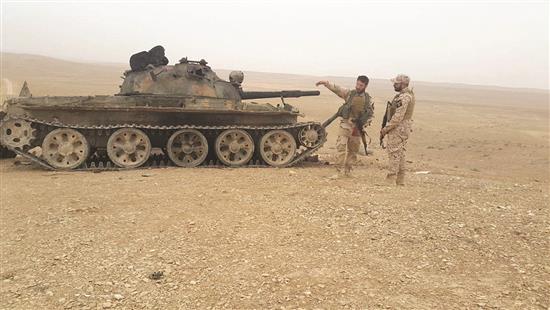 عنصران من «نسور الزوبعة» قرب دبابة مدمرة لـ «داعش» على أطراف حقل شاعر (سيف عمر الفرا)