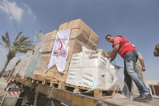 فلسطينيون يتفقدون المساعدات التركية التي وصلت عبر سفينة «لايدي ليلى» عند معبر كرم أبو سالم الفاصل بين الأراضي المحتلة وقطاع غزة أمس (رويترز)
