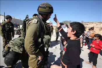 فلسطيني يرفع شارة النصر في وجه جندي للاحتلال في بلدة المعصرة أمس.
